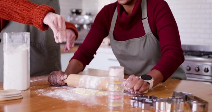 Two women at home, African American woman using rolling pin after helper sifting flour for cookies