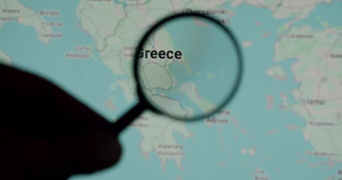 Hand with a magnifying glass moving over a map of Greece on a computer screen, symbolizing research, travel planning, or geopolitical analysis of the European country and its capital, Athens