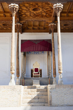 Throne room of the Ark Fortress in Bukhara with ornate golden throne under carved wooden columns and ceiling. Historic royal seat of the emirs of Bukhara, ideal for travel and heritage publications.