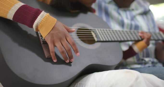 African American senior man guiding girl fingers resting, strumming guitar, pointing frets on couch