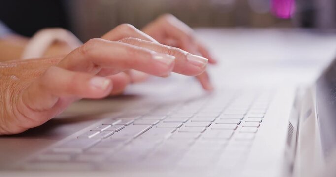 African woman typing on laptop at desk with wristband, fingers hovering pressing keys entering data