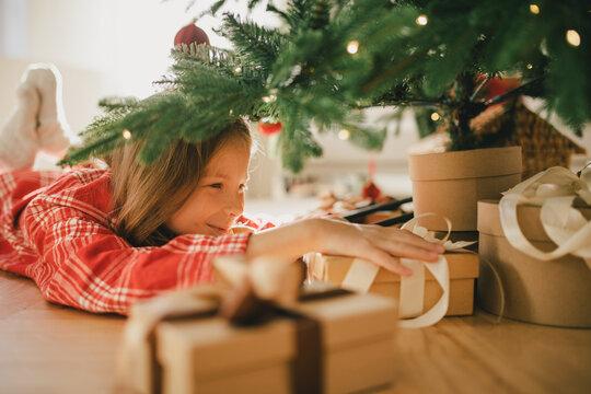 Cute 7-years old girl looking for a present under Christmas tree.