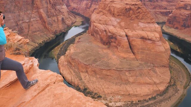 Adventurous female photographer capturing stunning landscape of horseshoe bend on colorado river, standing on edge of canyon cliff for perfect shot of this iconic destination