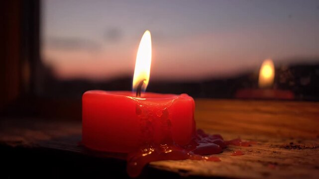 Red Candle Burning at Dusk Window Reflection - A single red candle burns brightly on a wooden surface, with its flame casting a warm glow.