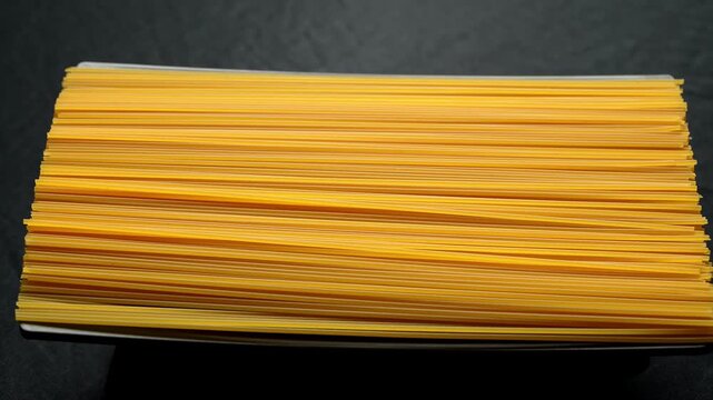 Rotating stack of uncooked dry spaghetti pasta noodles on dark backdrop.