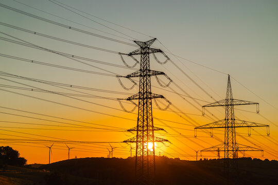 High-Voltage Pylons and Wind Turbines at Sunset