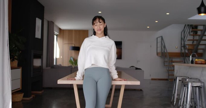 African American woman in hoodie and leggings at home hands on table, leaning, folding arms, posing