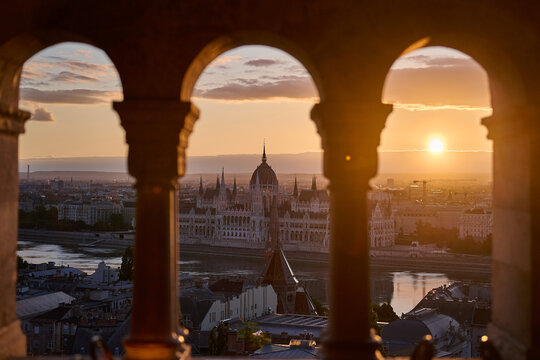 Hungarian Parliament Building and Budapest cityscape framed by stone arches of Fisherman's Bastion during sunrise in Budapest, Hungary