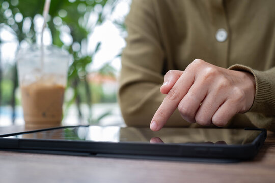 Close-up of a hand tapping a tablet touchscreen beside iced coffee in a modern cafe, representing digital interaction, mobile technology, online services, productivity, and convenient user experience.