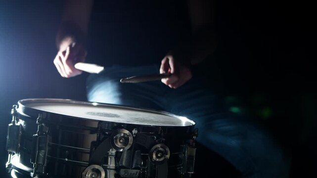 Drummer plays drum rudments, practise rolls, on snare drum. Dark background, high contrast. Medium shot, dramatic backlight. Shot with high shutter angle for visibly smooth, fluid stick motion. 