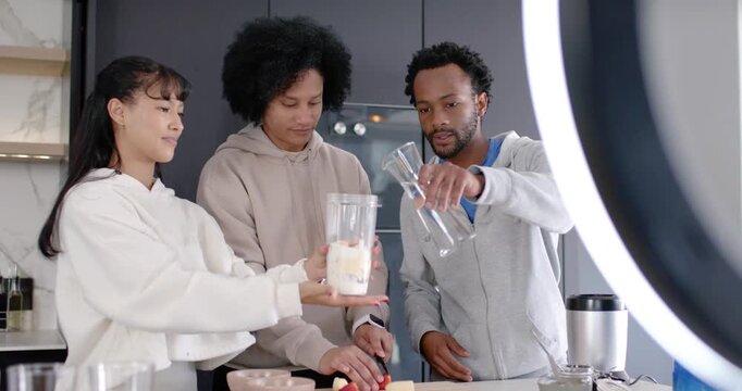 Diverse friends filming recipe with ring light filling blender jar slicing fruit and pouring water