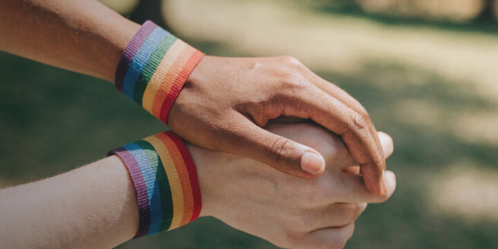 Pride in LGBTQ with love and gender equality with two people's hands holding each other wearing rainbow bracelets