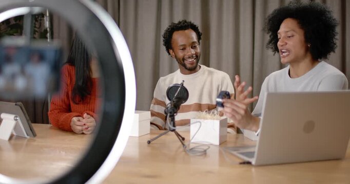 Diverse coworkers unboxing and demoing device on table in studio with smartphone starting recording