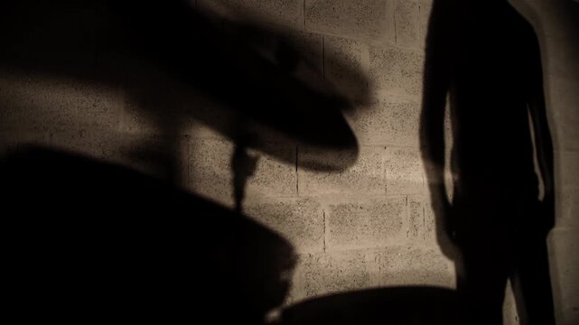 Shadow projected on wall of drummer sitting at drumkit and performing drum solo. Fluid, slow motion. Fixed tripod shot. Stylized, abstract, creative background. empty negative space