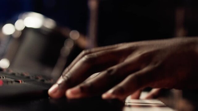 Close-up of hands playing fast keyboard passage, in live concert performance, with drummer visible playing in background, out of focus. Smooth handheld movement, low-key, high contrast