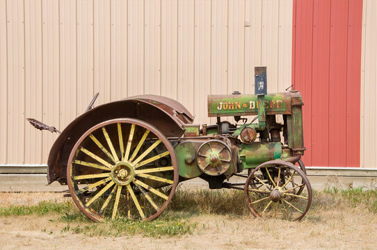 IRRICANA, CANADA - 08 AUGUST 2026: An antique green and yellow John Deere Model D tractor with spoked steel wheels parked against a rustic corrugated metal barn wall.