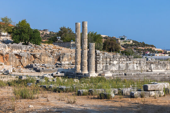Weathered broken stone columns rise from Patara ruins against a bright blue sky. Patara was an ancient and flourishing maritime and commercial city that was for a period the capital of Lycia