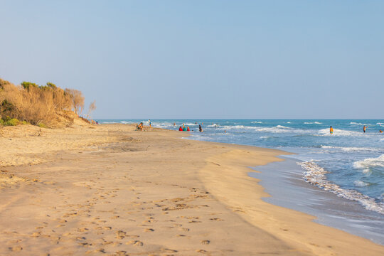 Kumluova Plaji, Patara, Turkey. A wide sandy beach with footprints leading to the shoreline where people enjoy gentle waves, sun, and open sky