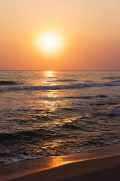 An atmospheric vertical photo capturing tranquility, natural beauty and the peaceful essence of summer evening. Serene sunset illuminating ocean waves with vivid warm tones and reflecting golden light