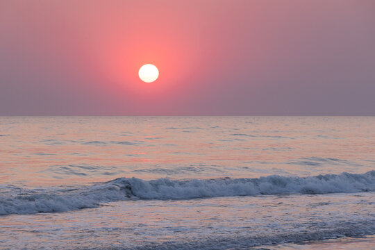 A serene photography of the sea at sunset, showcasing calm waves and a pink sky. Perfect depiction of tranquility, natural beauty and retreat during golden hour