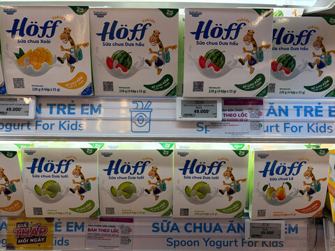 A display of yogurt products for children features various flavors, including fruit designs on the packaging. Bright and colorful, the boxes appeal to kids. Labels in Vietnamese indicate purpose 