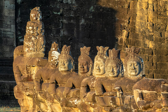 Asuras head statues in a row at Angkor Thom South gate, demon faces at sunset in Angkor, Siem Reap, Cambodia