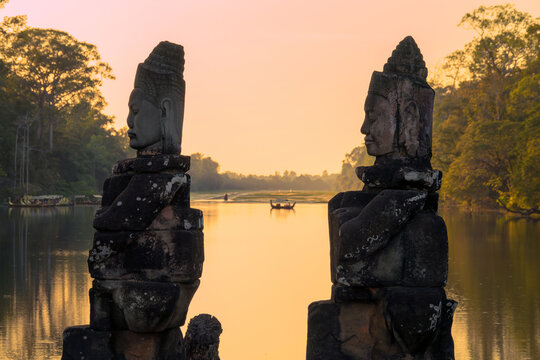 Deva head statues at Angkor Thom South gate, serene Buddha face at sunset in Angkor, boats on ancient moat with water reflections, Siem Reap, Cambodia