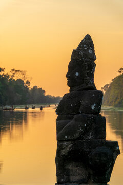 Deva head statue at Angkor Thom South gate, serene Buddha face at sunset in Angkor, ancient moat with water reflections, Siem Reap, Cambodia