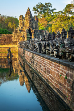 Row of Devas head statues at Angkor Thom South gate, serene Buddha faces at sunset in Angkor, ancient moat with water reflections, Siem Reap, Cambodia
