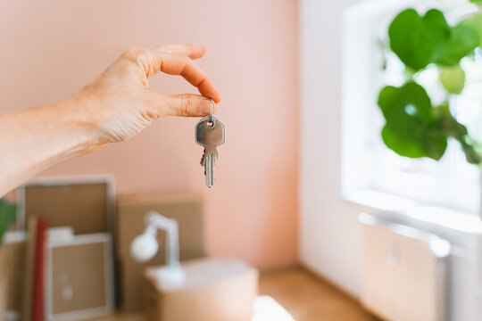 Hand holding keys with moving boxes indoors in new apartment. Relocation and residential property purchase commercial concept.