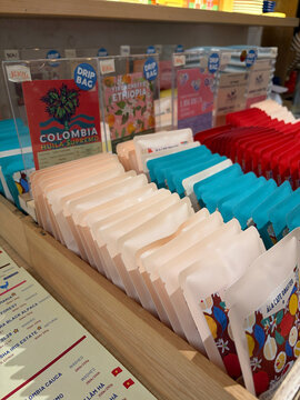 A display of various coffee packages lined up on shelves. The packages feature bright colors including red, blue, and white.