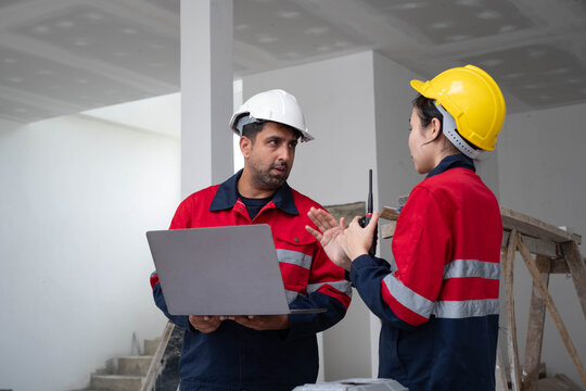 Construction workers in hard hats discuss a project while using a laptop and radio at an active worksite, showing teamwork, communication, engineering, safety, planning, and field management.