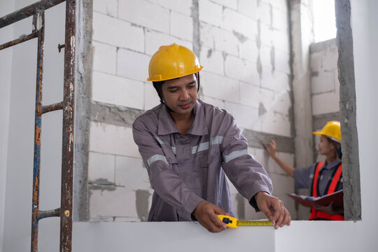 Construction workers measuring a new interior wall with a tape measure, highlighting building inspection, renovation, teamwork, safety, and professional craftsmanship on an active job site.