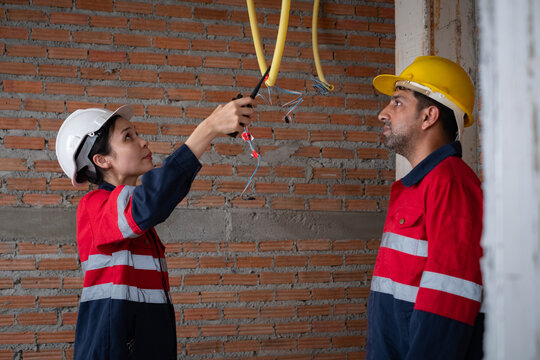 Professional electricians inspecting electrical wiring at a residential construction site, wearing safety helmets, protective uniforms, highlighting teamwork, electrical installation, workplace safety