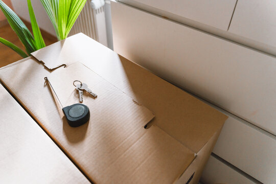 House keys and a retracted measuring tape rest on top of closed cardboard moving boxes in a bright room. Home renovation planning and successful relocation real estate concept.