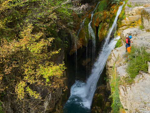 aerial view of a serene waterfall in a canyon with lush vegetation and climbing gear-wearing individuals enjoying outdoor recreation and canyoning activities under.
