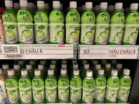 A shelf in a grocery store displays multiple bottles of Asian milk drinks. Each bottle has a green cap and vibrant label design. The drinks are organized neatly, creating a colorful visual appeal.