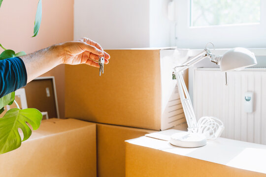 Hand holding keys with moving boxes indoors in new apartment. Relocation and residential property purchase commercial concept.
