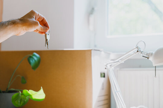 Hand holding keys with moving boxes indoors in new apartment. Relocation and residential property purchase commercial concept.