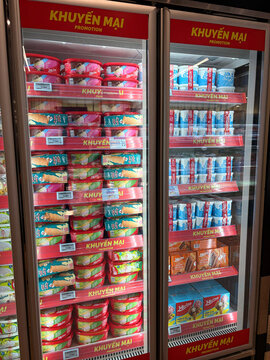 A display of frozen food products visible in glass refrigerator doors. Shelves are stocked with colorful packaging of various snacks and meals. Products include ice cream, meat, and prepared meals.