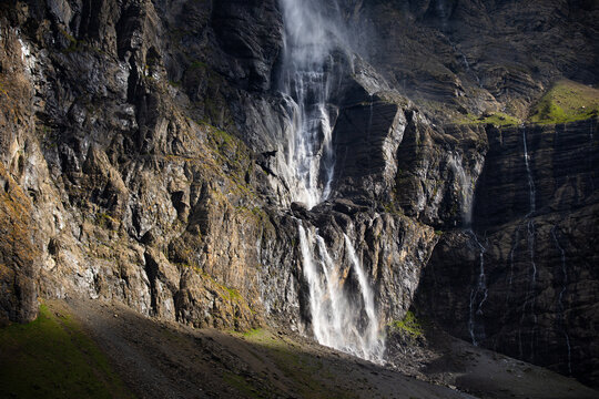 serene waterfall cascading down rocky cliffs in a mountainous landscape from below, looking up the cliff with green and brown vegetation and white rocks creating a dramatic and dynamic view.