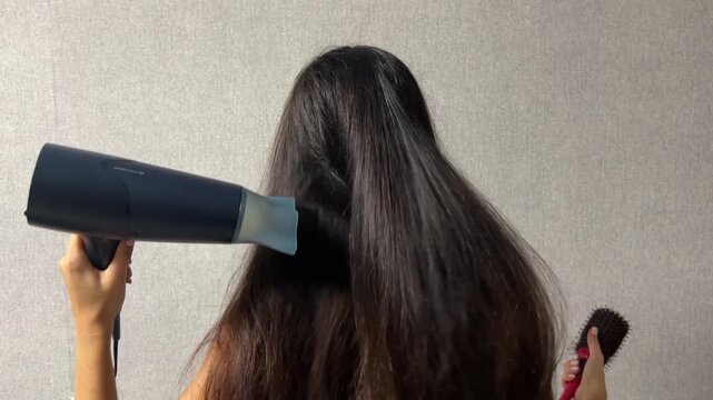 Woman drying her long hair with a hair dryer at home during a daily hair care and beauty routine