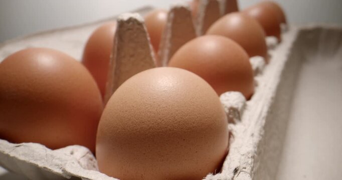 Cinematic push-in over cardboard package containing eggs, filmed with a probe lens. The close-up perspective highlights the natural texture of the eggs, creating a visual suitable for food production
