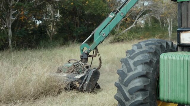 Tractor with Boom Flail Mower Clearing Tall Grass and Weeds Beside Road