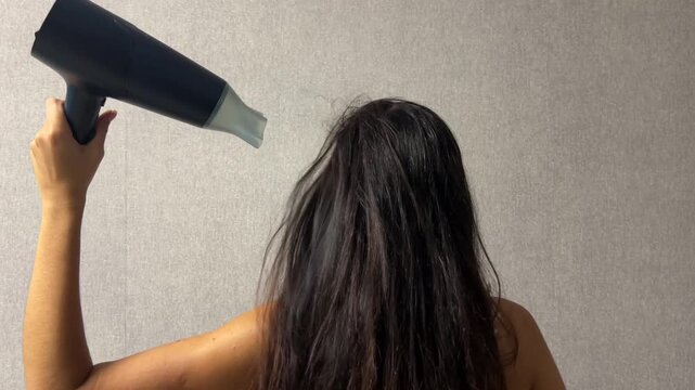 Woman drying her long hair with a hair dryer at home during a daily hair care and beauty routine