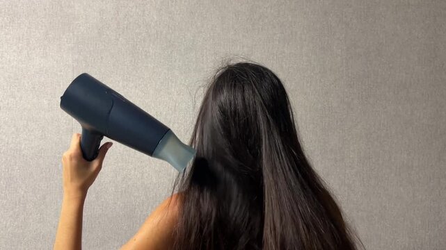 Woman drying her long hair with a hair dryer at home during a daily hair care and beauty routine