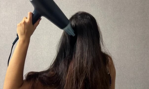 Woman drying her long hair with a hair dryer at home during a daily hair care and beauty routine