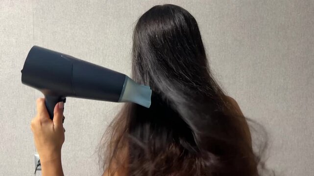 Woman drying her long hair with a hair dryer at home during a daily hair care and beauty routine