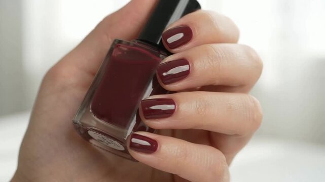 Woman admiring burgundy nail polish on fingertips in natural light