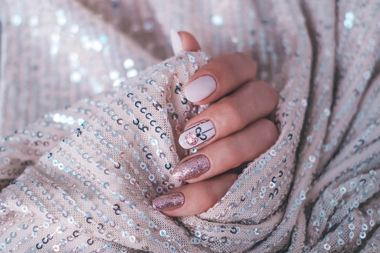 A beautiful oval-shaped Christmas manicure set against a glittery background. A winter trend featuring beige gel polish (Shellac). Space for text.